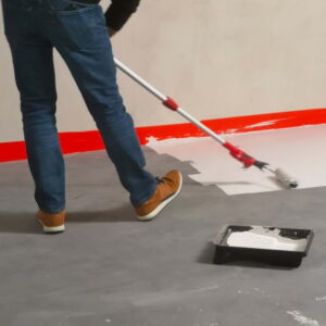 Une personne repeint le sol de son garage avec de la peinture pour sol blanche , une perche et un rouleau
