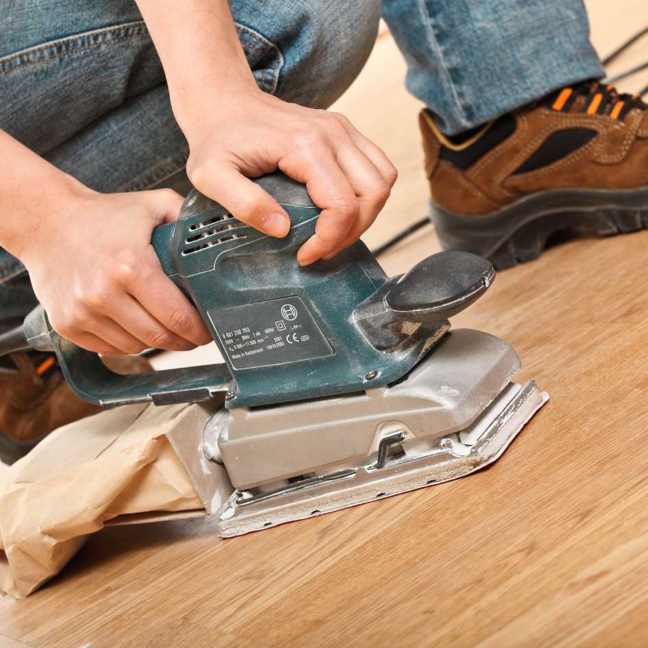 Homme qui ponce un parquet à l'aide d'une ponceuse électrique