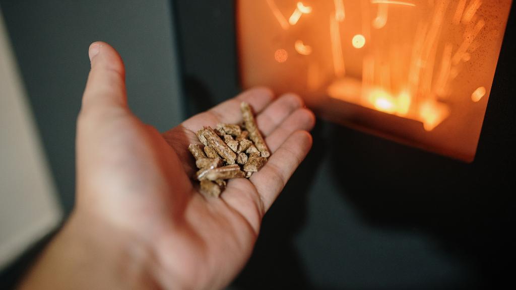 Main avec des pellets de bois devant un poêle à pellets