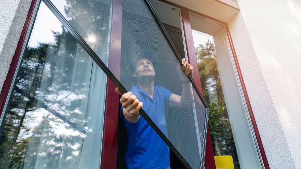 Homme qui pose un cadre de moustiquaire sur une fenêtre