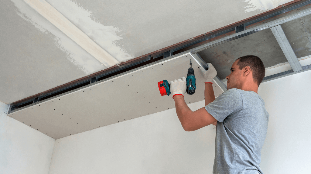 un ouvrier fixe une plaque de plâtre sur un faux plafond