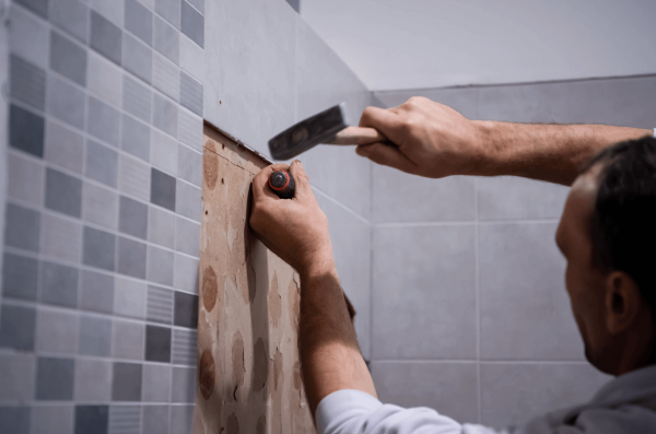Un carreleur qui enlève de la faïence sur un mur