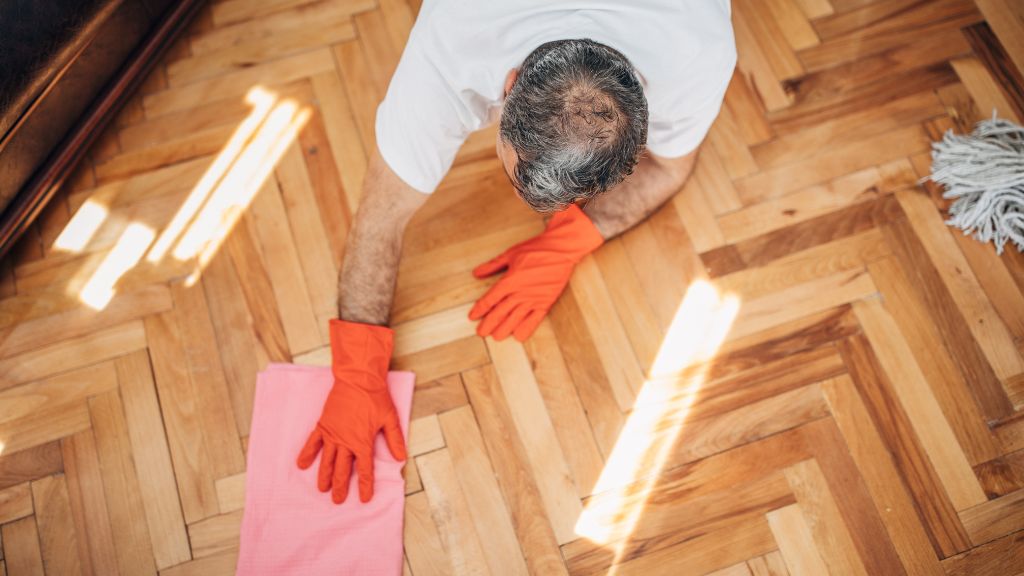 Homme qui nettoie un parquet avec des gants et un chiffon microfibre